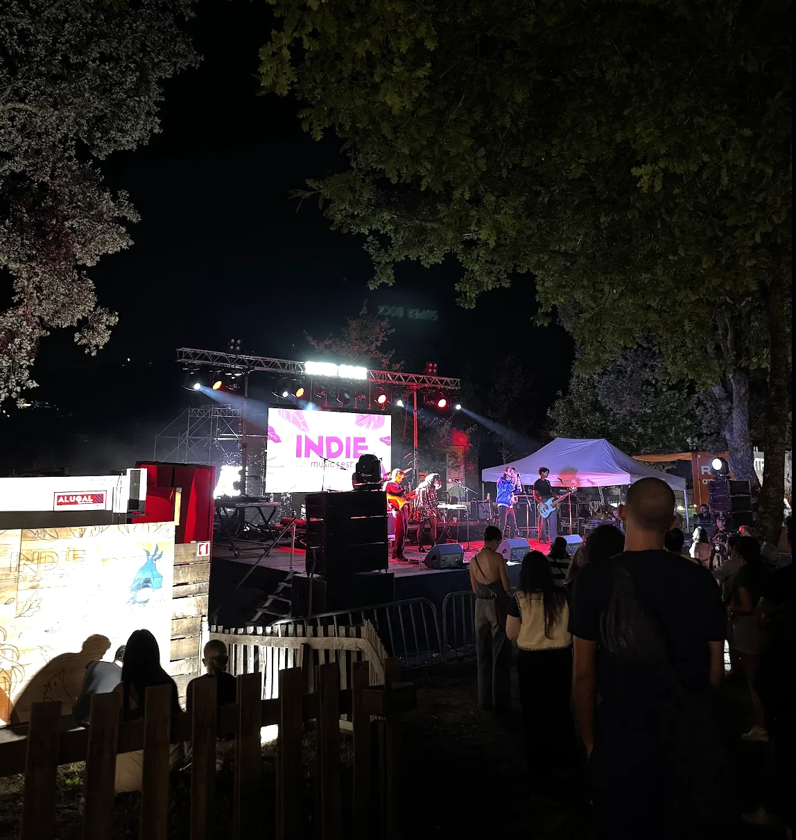 Band on stage and audience watching a concert among the trees at Indie Music Fest at night