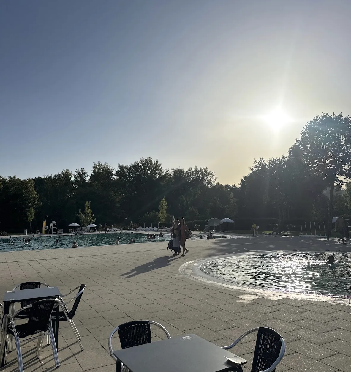 Pools and terrace at Piscina Verde in the late afternoon, with swimmers and trees around