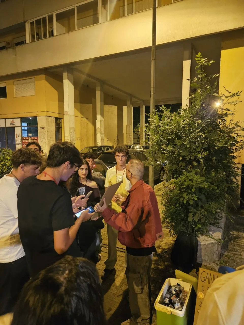 Talking to a group of first-years, some with phones in hand, next to the sign and the cooler