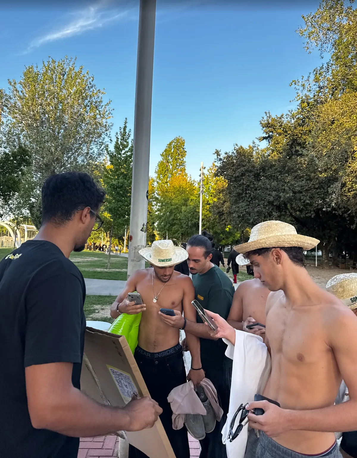 Students in hats downloading the app on their phones next to the sign with the QR code, on the way to the pools