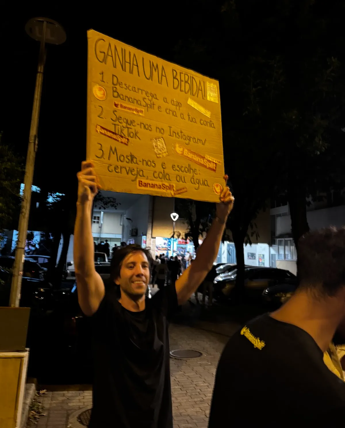Nuno raising the "Win a drink!" sign above his head, in the street at night