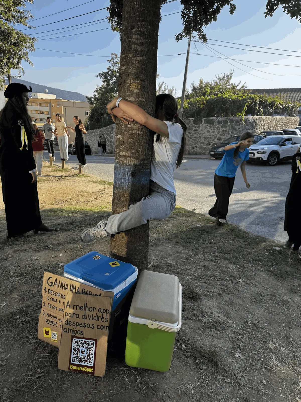 A student climbing a tree next to the BananaSplit coolers and sign during a praxe